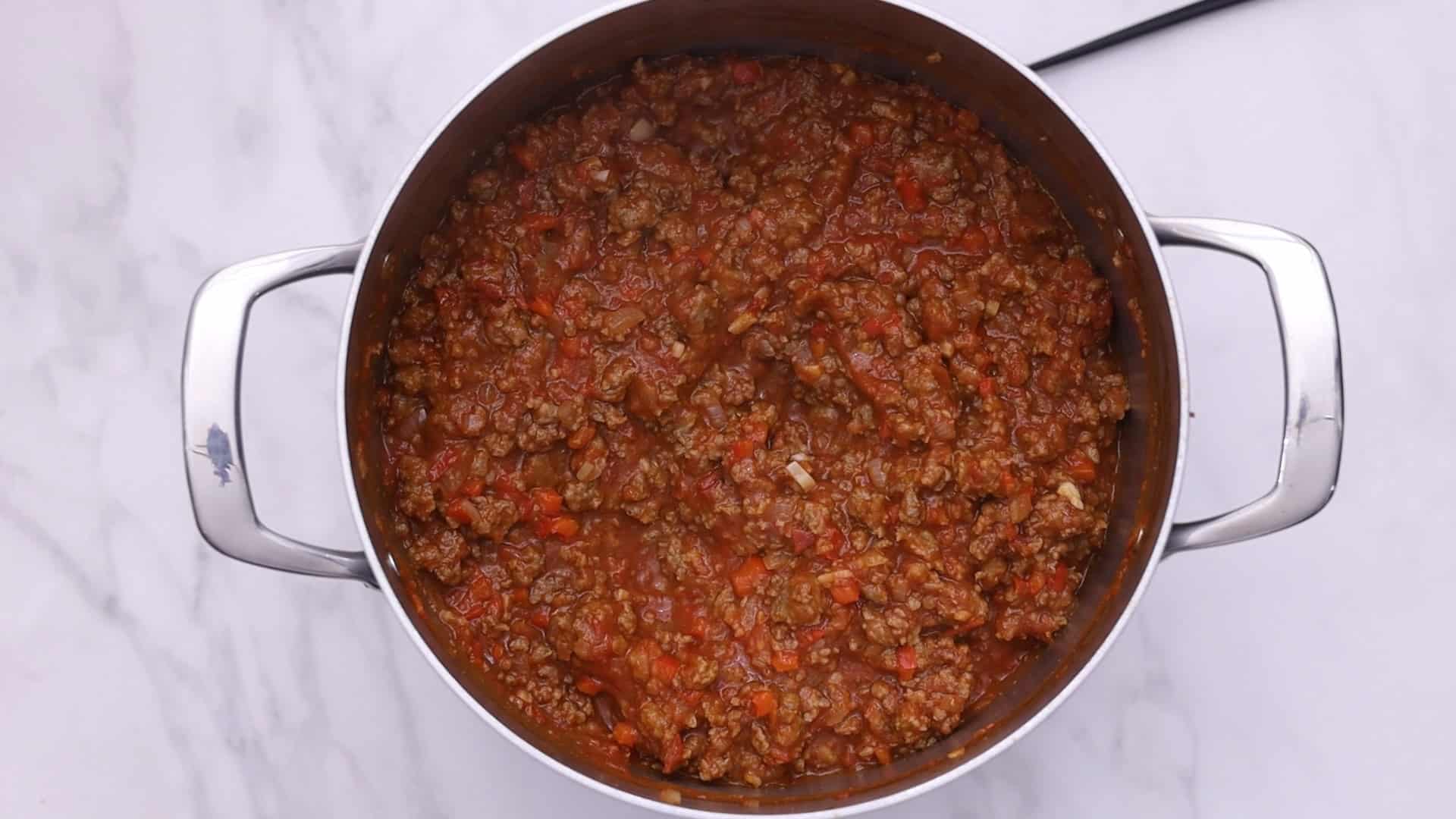 Añadir los tomates, el azúcar, los copos de pimiento rojo y la pimienta negra; cocer a fuego lento.