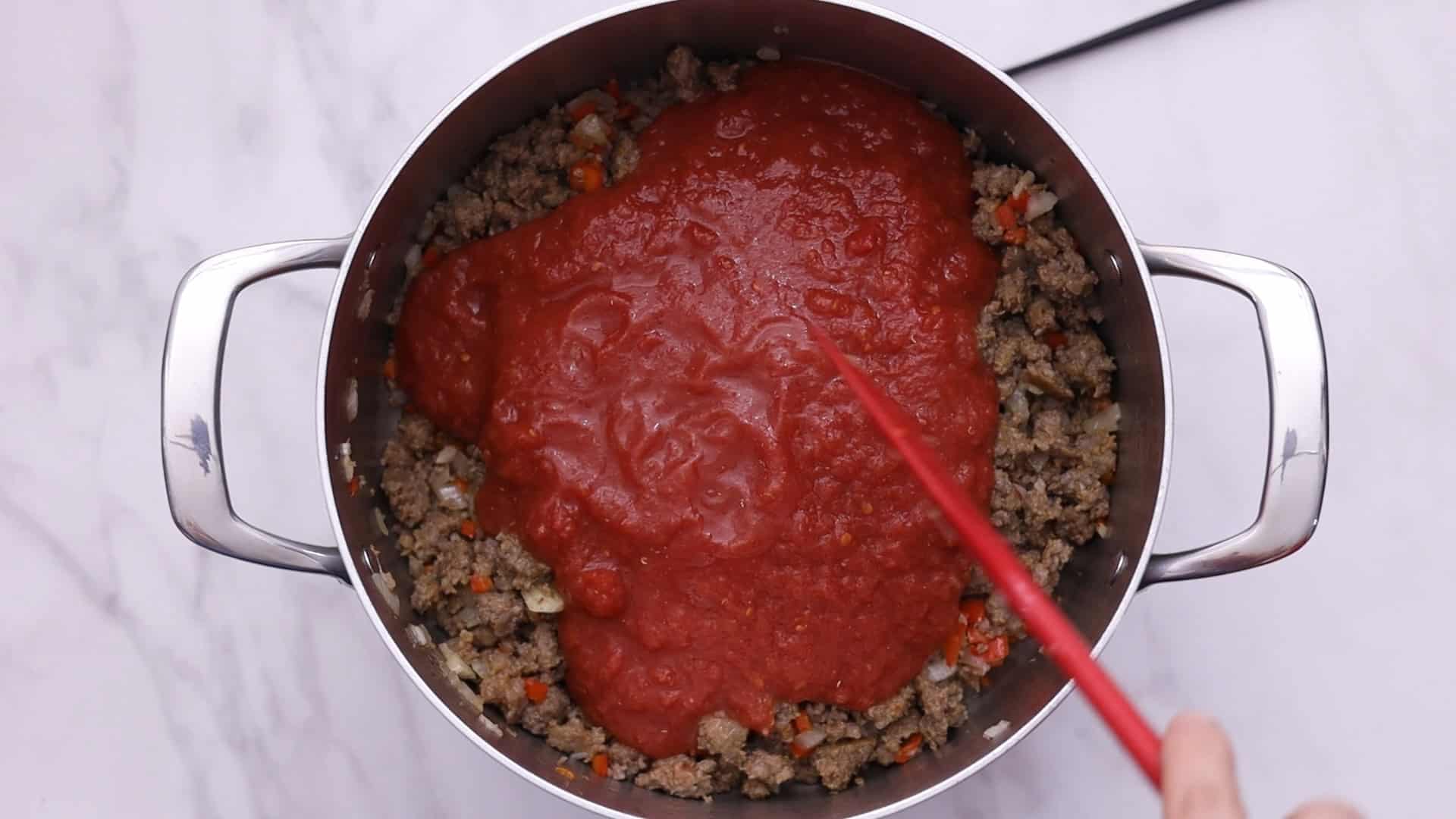 Añadir los tomates, el azúcar, los copos de pimiento rojo y la pimienta negra; cocer a fuego lento.