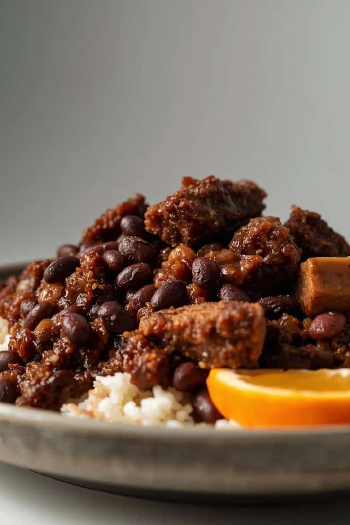 Low side-angle food photography showing feijoada, black beans and meats layered thickly,