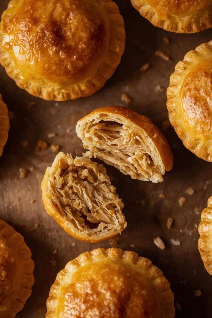 top view A close-up, detailed food photograph capturing Brazilian empadinhas de frango. The small, golden shortcrust pastries feature a glossy, perfectly egg-washed top. One empadinha is artfu (1)
