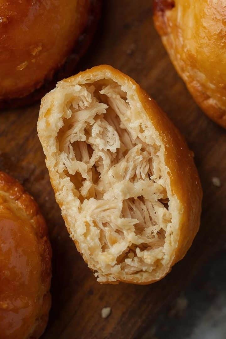 top view A close-up, detailed food photograph capturing Brazilian empadinhas de frango. The small, golden shortcrust pastries feature a glossy, perfectly egg-washed top. One empadinha is artfully