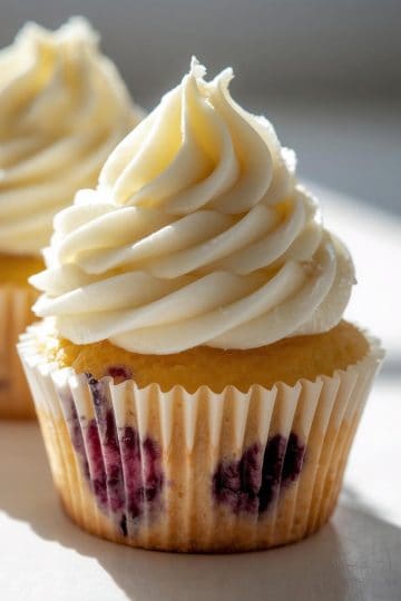 Blueberry lemon cupcakes with cream cheese frosting, bright natural window light, soft moist crumb with juicy blueberries, airy frosting, slightly uneven